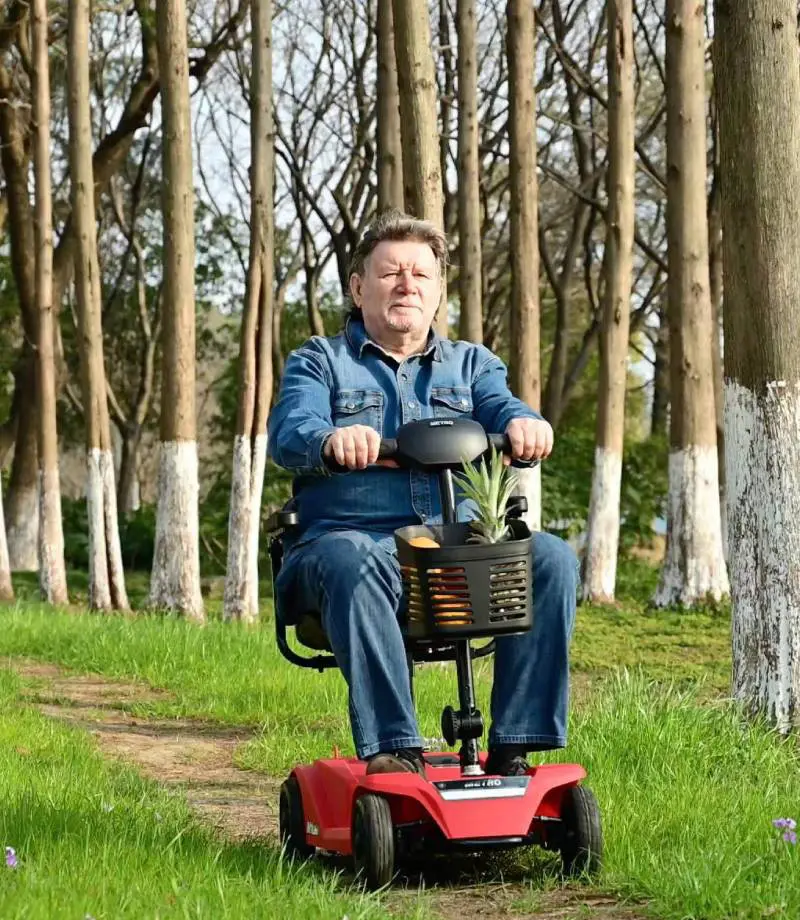Man riding a red mobility scooter in a wooded park.