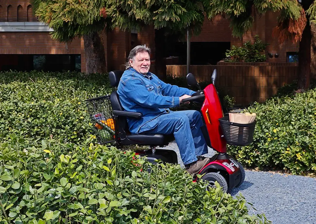 Person smiling on a red mobility scooter in a garden.