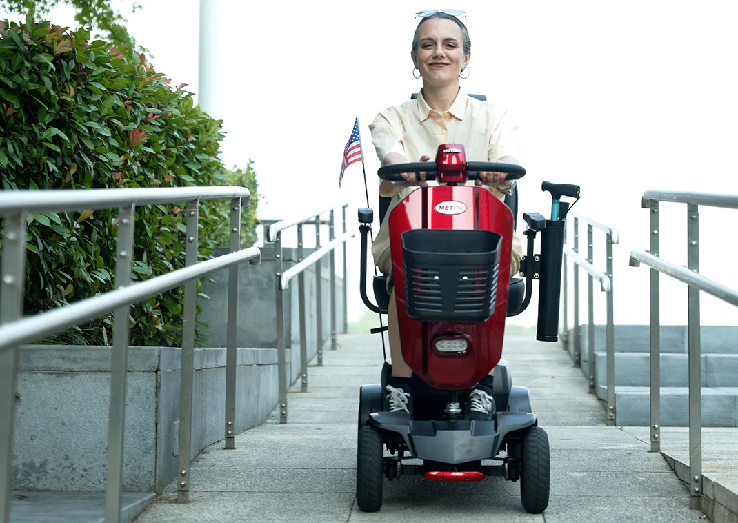 Smiling elderly woman riding a red mobility scooter outdoors.