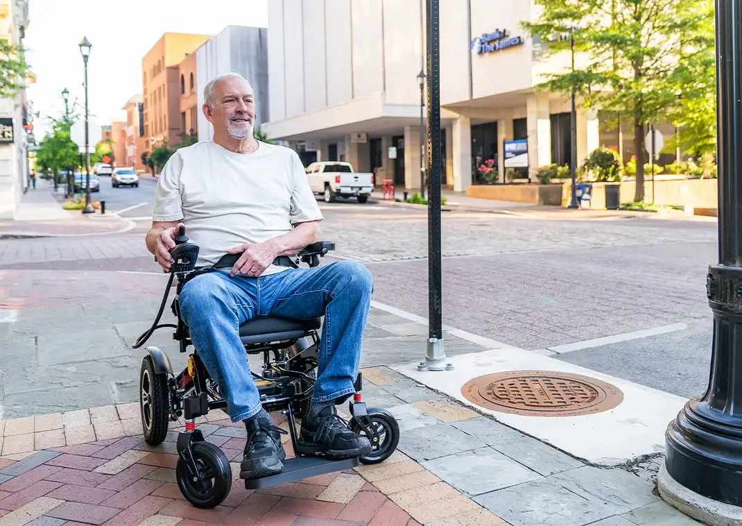 An elderly man smiling in a motorized wheelchair on a city sidewalk.