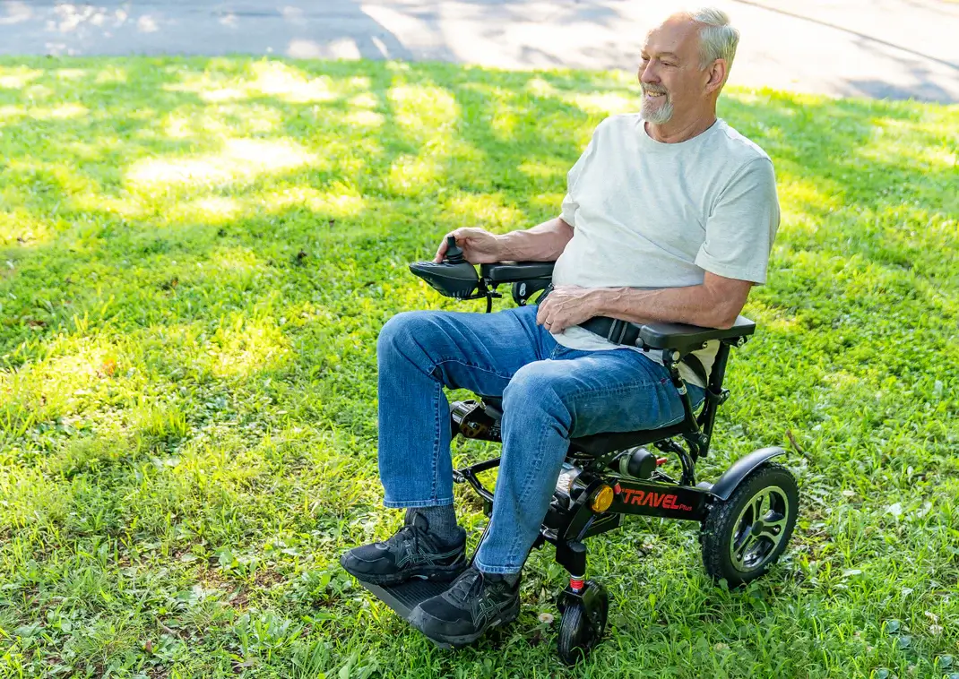 Elderly man enjoying a sunny day in a powered wheelchair outdoors.