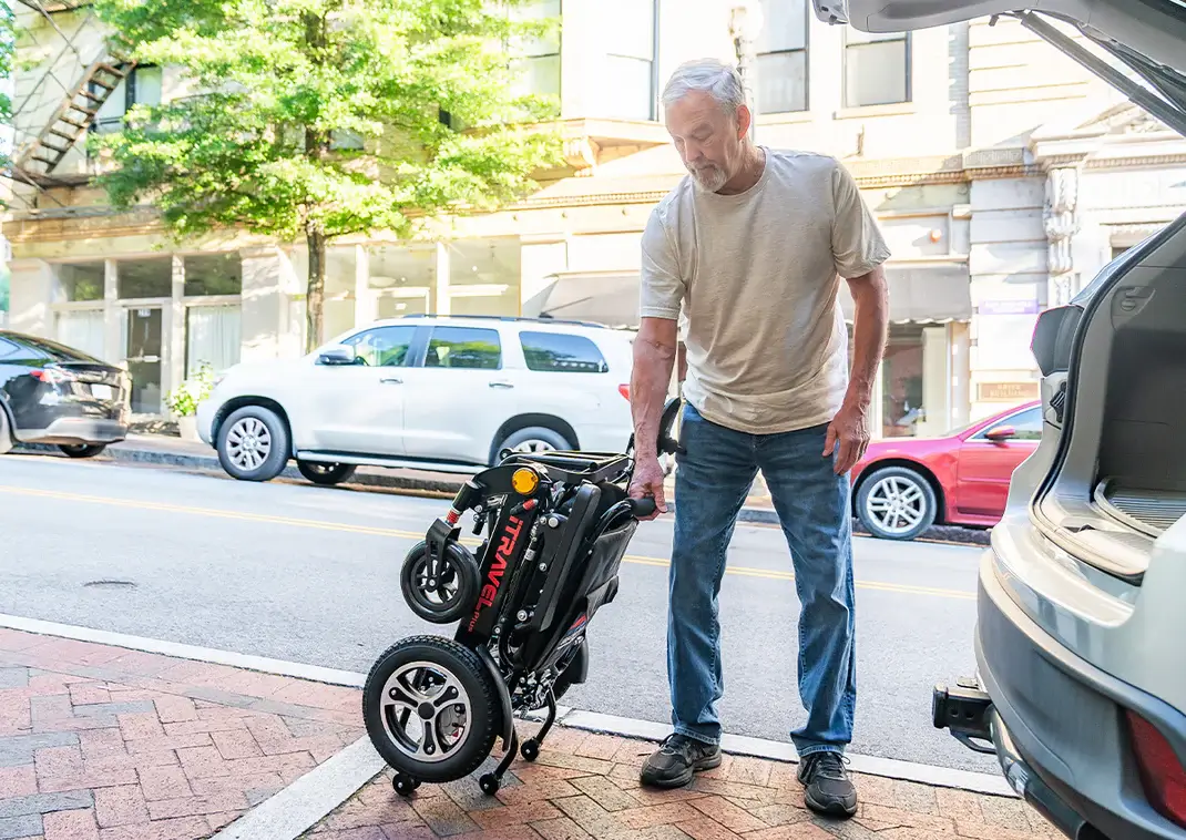 An elderly man lifting a folded stroller on a sidewalk.