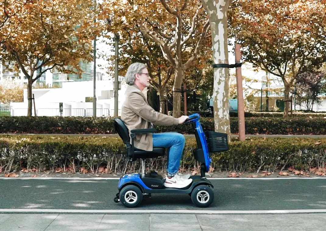 Older woman riding a mobility scooter outdoors on a path.