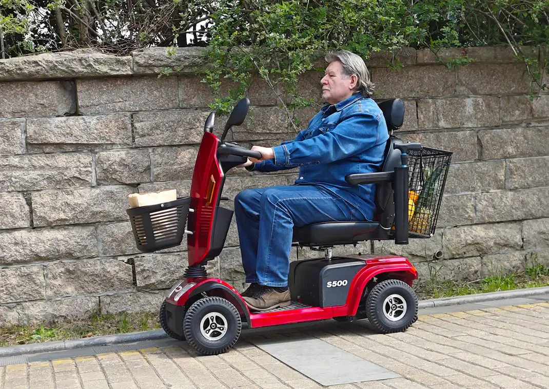Elderly person riding a red mobility scooter outdoors.