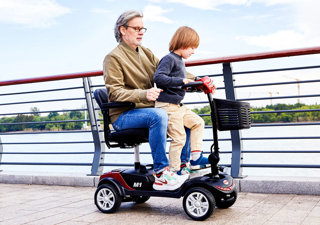 Elderly man and child enjoying a ride on a mobility scooter by the waterfront.