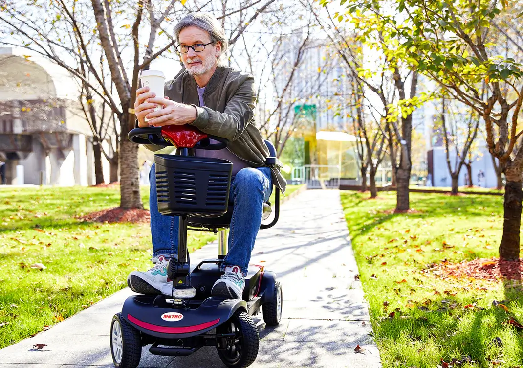 Young man using a mobility scooter outdoors on a sunny day.