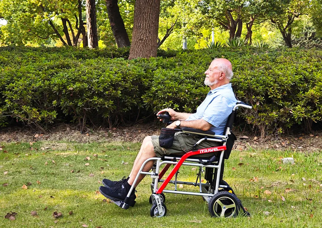 Elderly man resting in a wheelchair outdoors in a park.